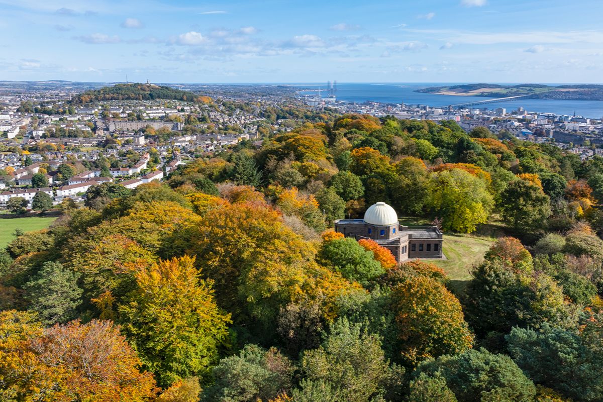 Trees surrounding a domed observatory. with a cityscape and body of water in the distance.