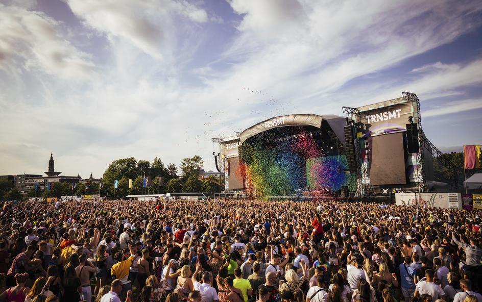 An outdoor music festival with a large crowd facing a stage labelled 'TRNSMT', with colourful confetti being released.