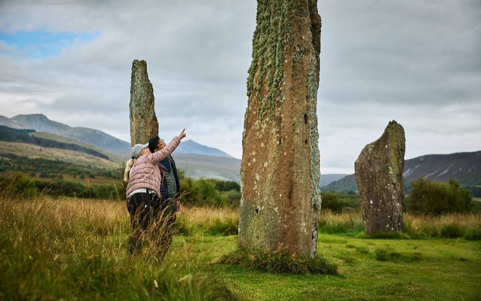 2 people looking at standing stones in grassy landscape.