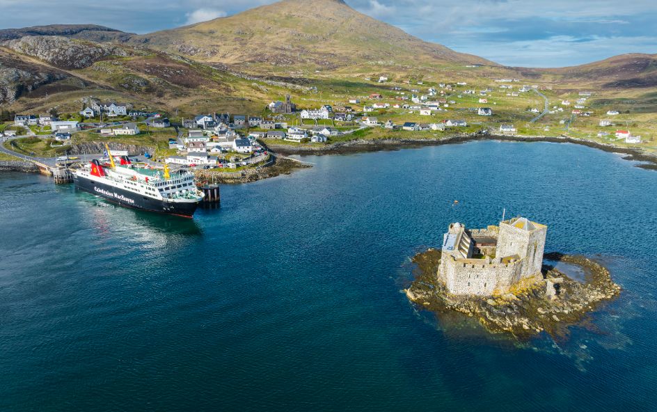 Ship decked at dock surrounded but town building and castle in middle of sea.