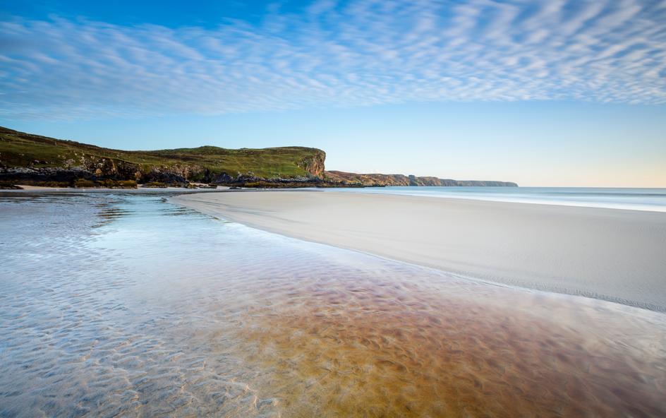 A sandy beach with cliffs in the background.