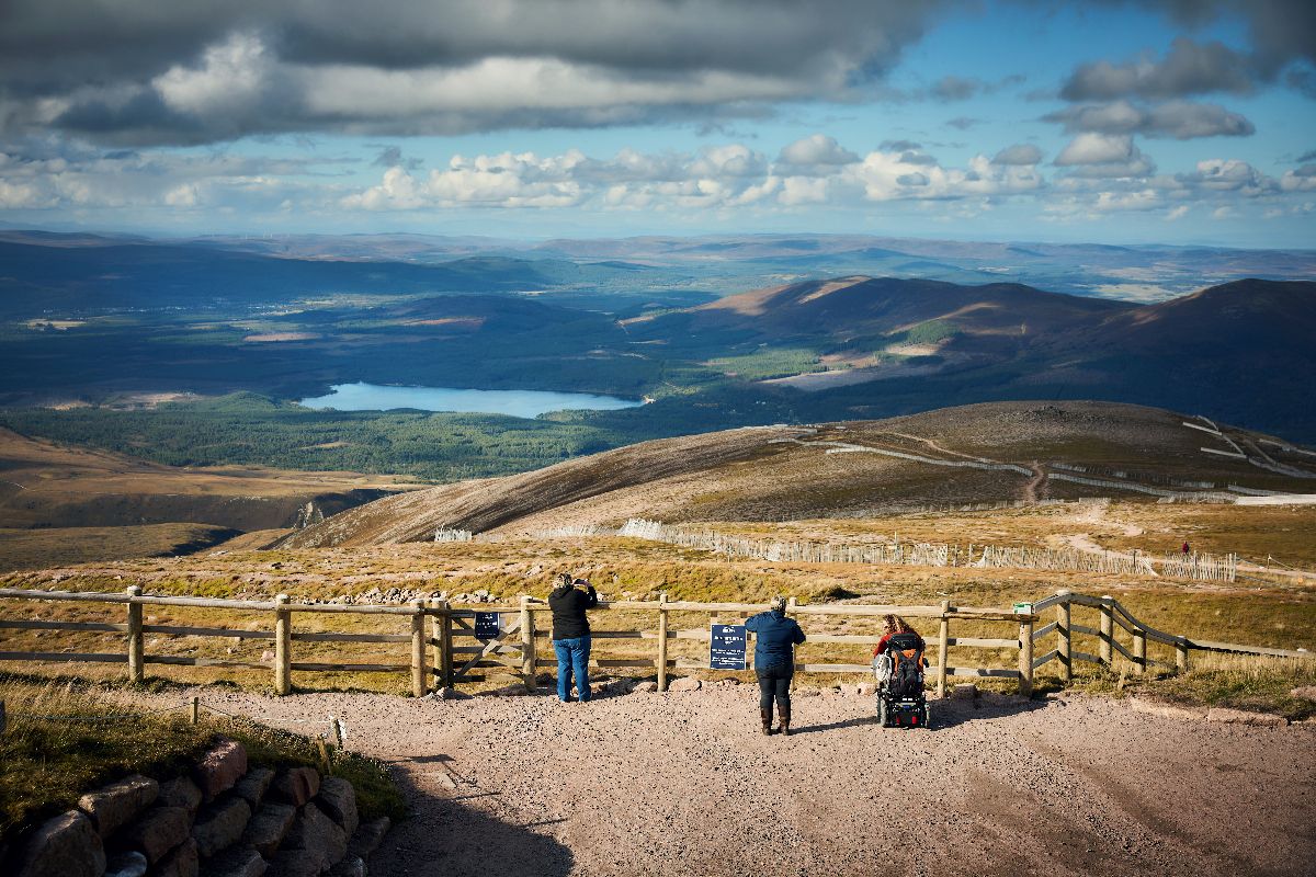Three people enjoying scenic mountain views overlooking a loch and rolling hills.