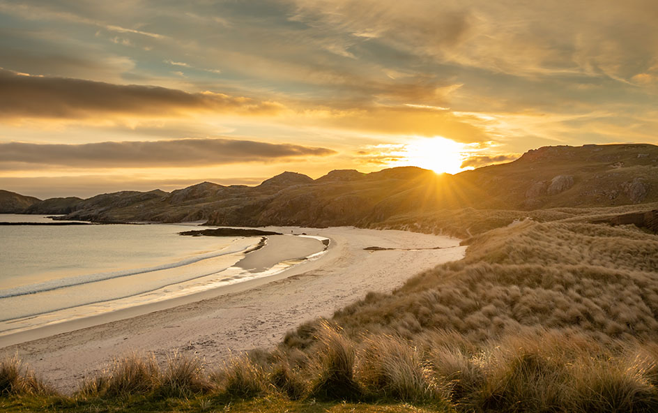 A beach with mountains and a sunset behind it