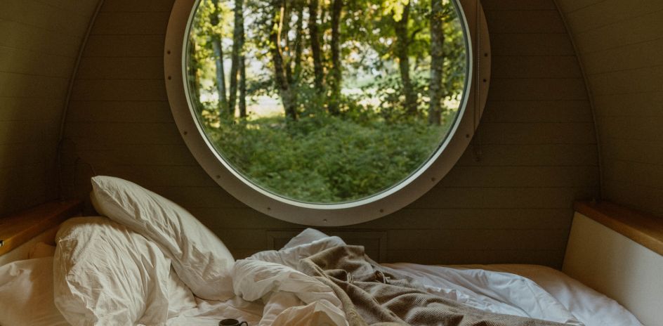 A peaceful view from a bed through a circular window, framing a serene scene of surrounding trees.