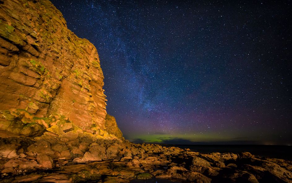 A rock formation with a starry sky and Northern Lights