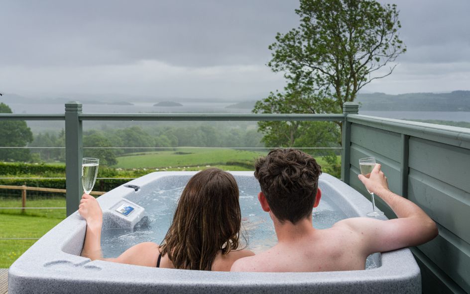 Two people relaxing in a hot tub looking out over a green landscape