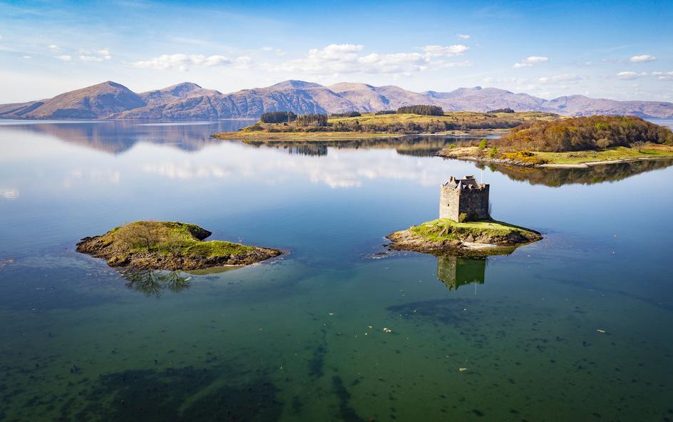 A calm sea loch with small islands, one featuring a historic stone tower.