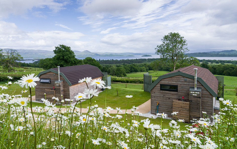 Two wooden glamping pods, with a view over water, mountains and a little island with trees.