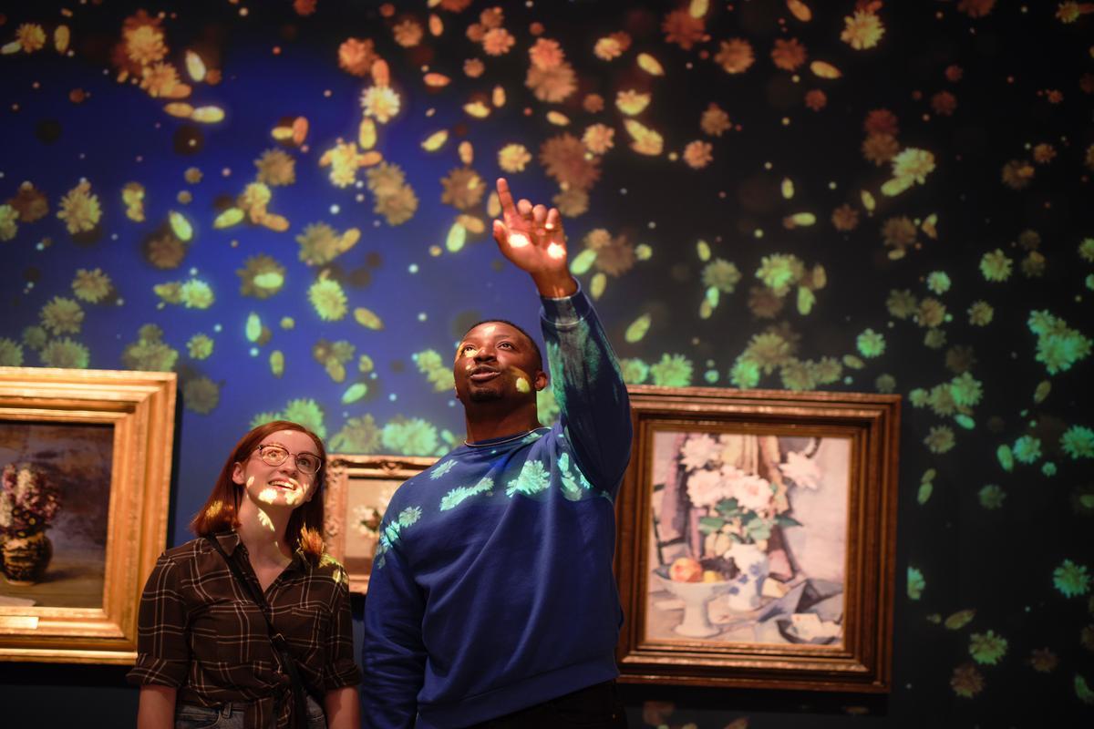 Two people looking at projections on a wall, in front of some artwork.