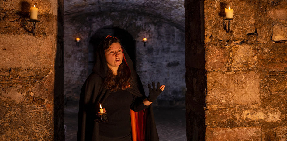 a storyteller with a cloak inside a candlelit stone building