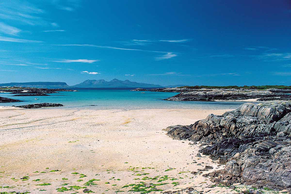 a golden beach with blue water and mountains in the far distance