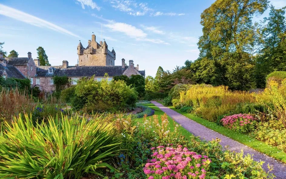 Turreted castle in grounds with colourful flowers.