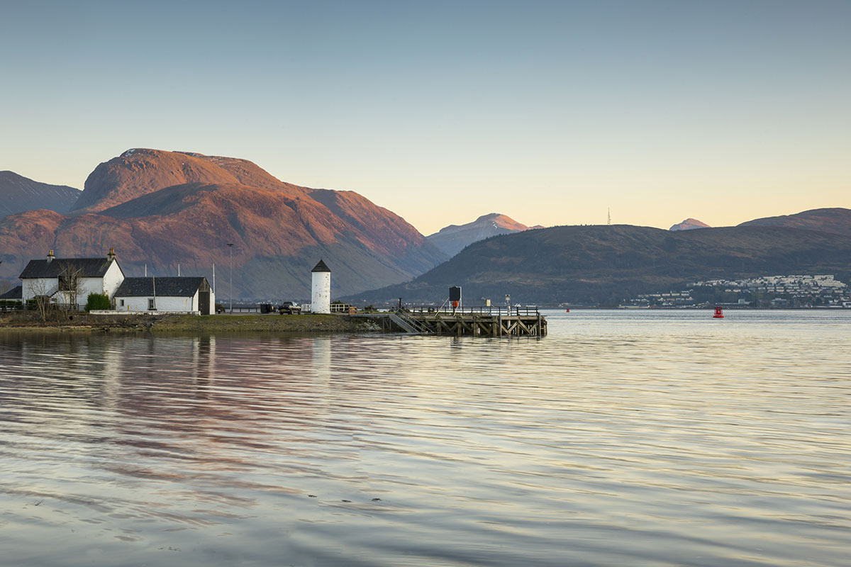 A loch with a peninsula with a building and a large mountain behind