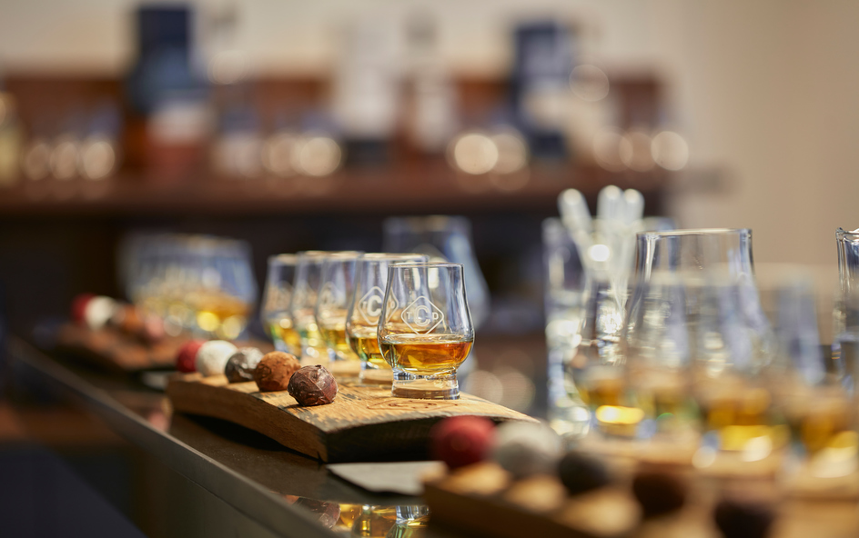 Several whisky glasses on a wooden board, with chocolate accompaniments.
