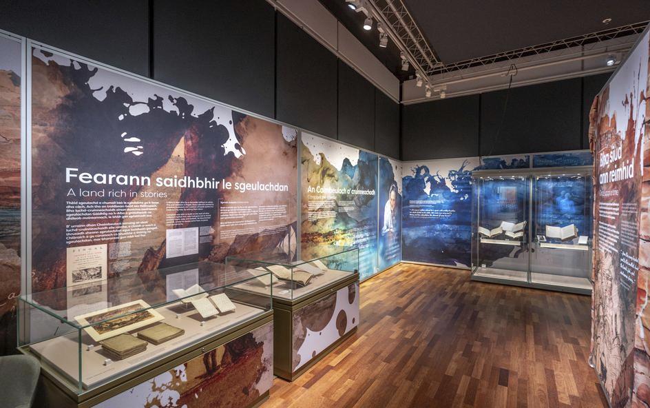 A museum exhibit containing books, featuring large informational panels with text and images in Gaelic and English.