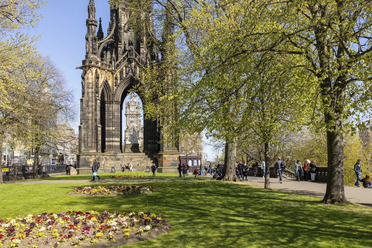 A historic monument in a park setting with green grass, flower beds and trees.
