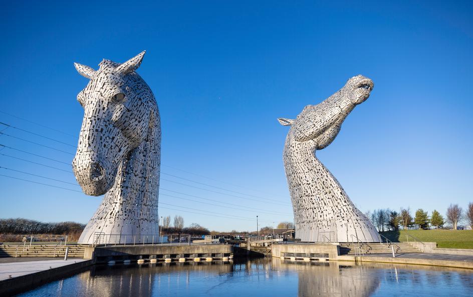 Two large steel horse heads next to water.