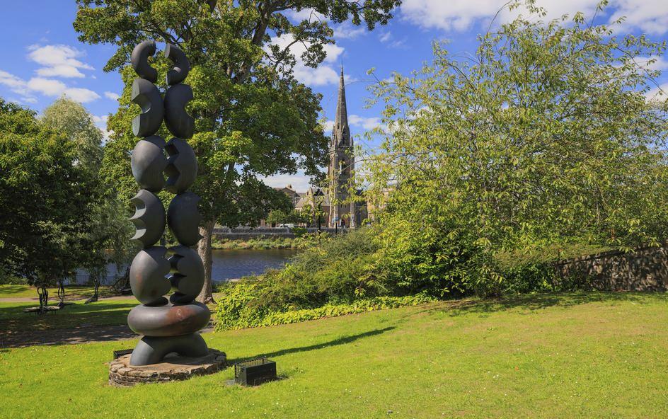 An outdoor park scene featuring a tall, abstract sculpture.