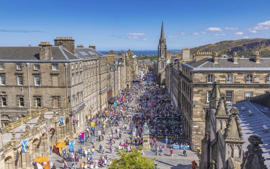 A bustling city street filled with people and performers, flanked by historic stone buildings.