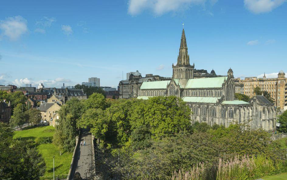 A large cathedral with a tall central spire surrounded by trees and historic buildings.