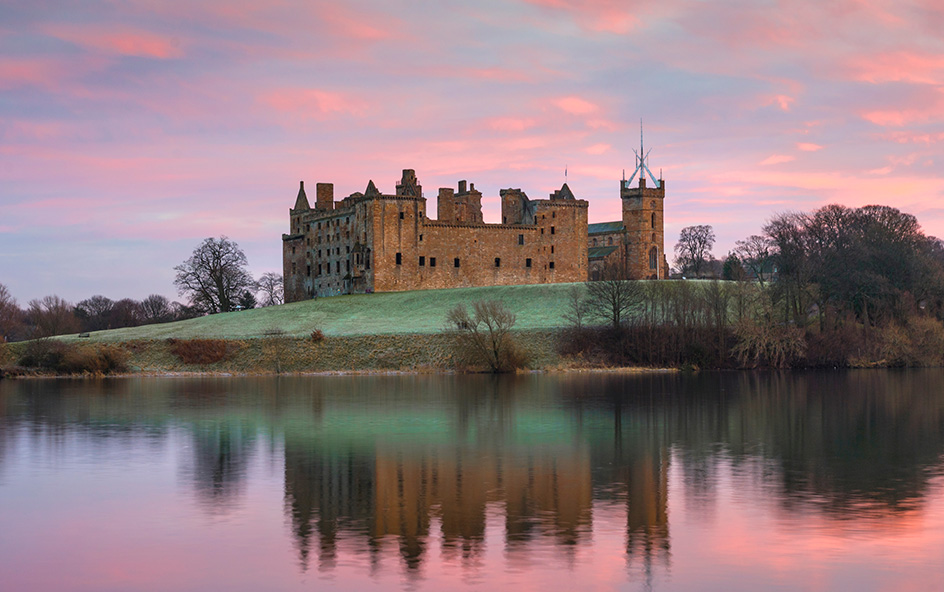 Palace mirroring on loch with pink cloudy sky.