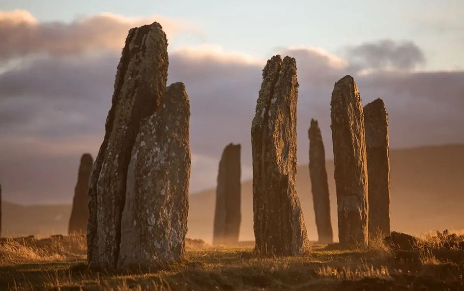 Tall, weathered standing stones arranged in a grassy field during sunset.