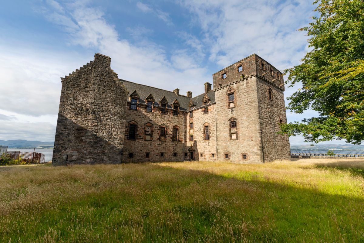 Large square stone castle with grassy field in front of it