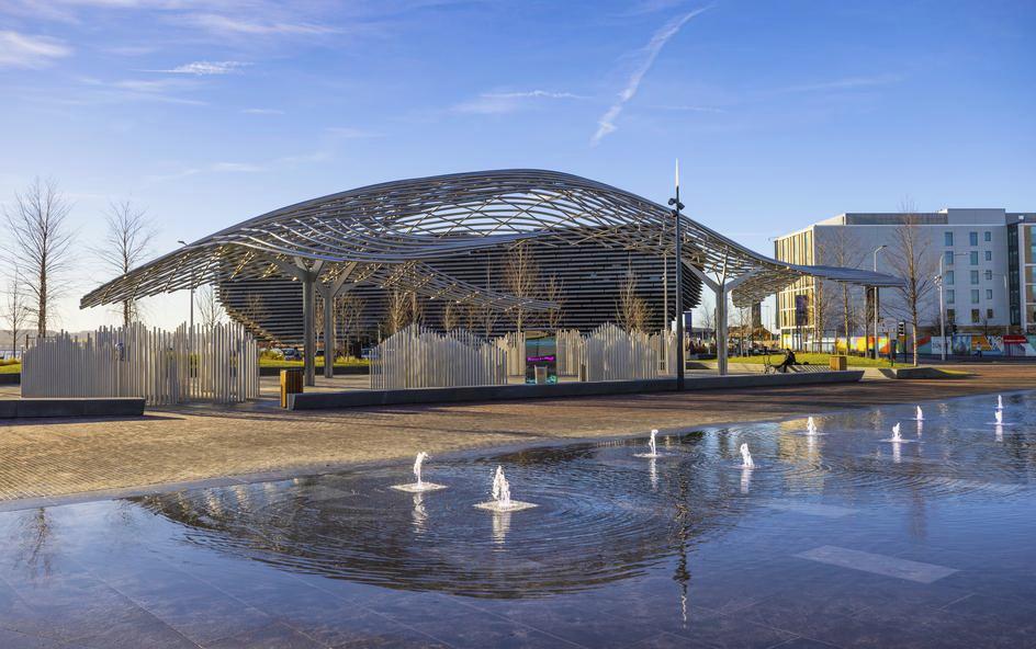 A large steel whale sculpture with water features in front of it.