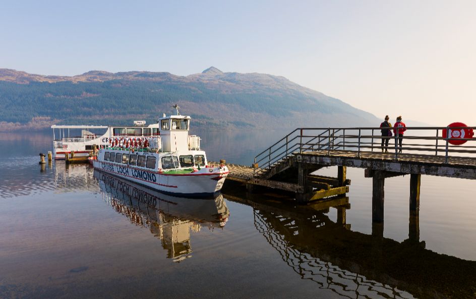 Cruise boat decked at harbour with mountain views behind.