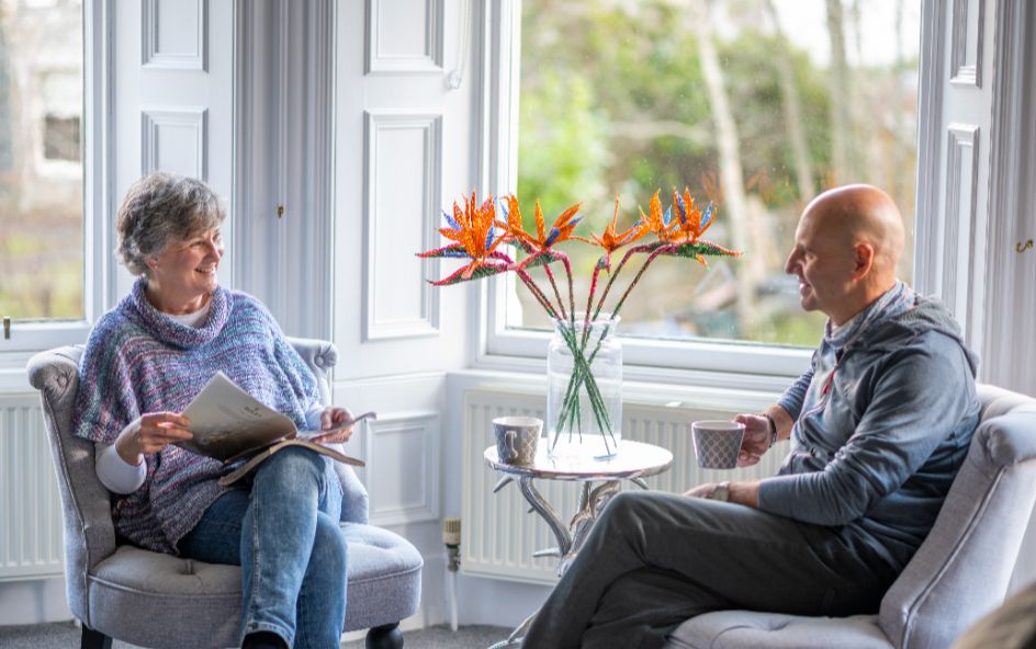 Two people sat beside window enjoying a cup of tea.