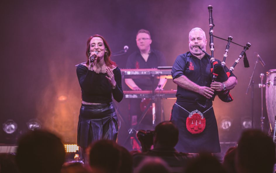 A live musical performance featuring a singer and a bagpiper on stage.