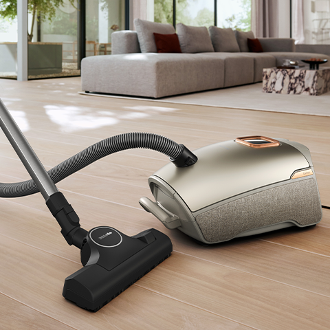 Miele Guard L1 sitting on hardwood flooring with living room in the background