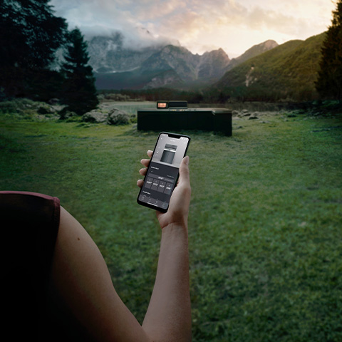Eine Hand, die ein Smartphone hält, mit dem eine Miele Outdoor-Küche gesteuert wird.
