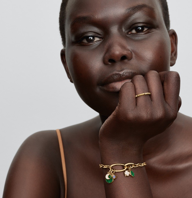 A model smiles in the sun as she wears Pandora ME link chain bracelets while holding a tangerine.