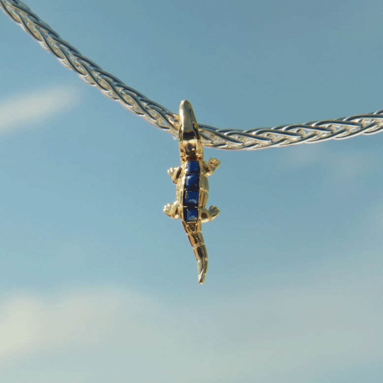 A gold and blue crocodile charm hanging from a silver chain