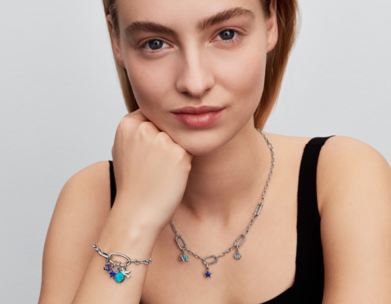Model care poartă o brățară și un colier Pandora ME din argint 925, cu zale și pandantive albastre.