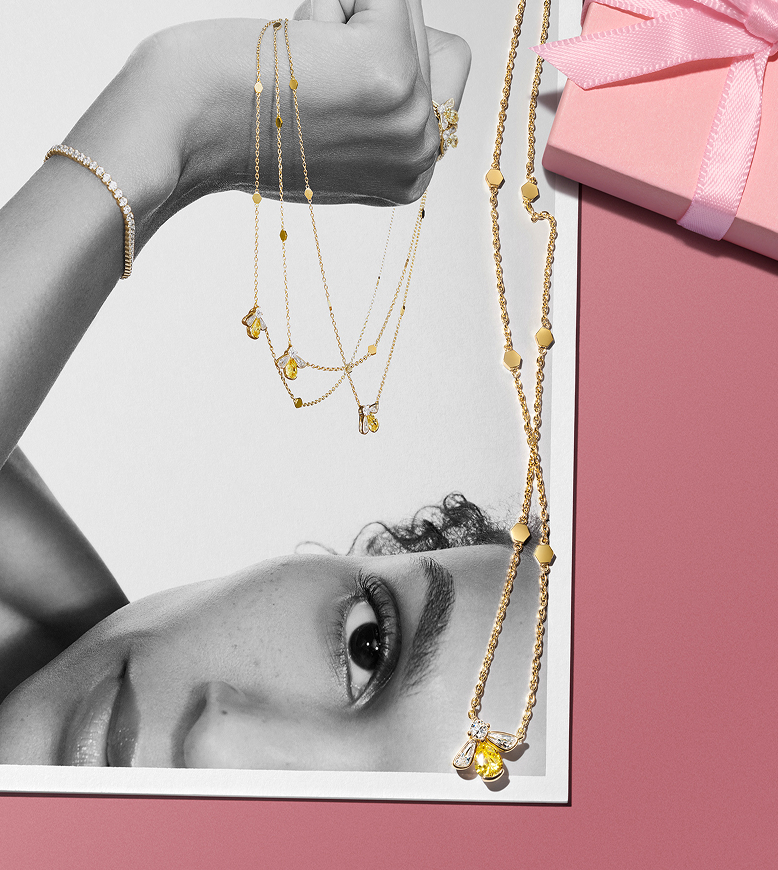 Timeless jewelled bee necklace placed over a photo of a model holding several of the same necklaces.