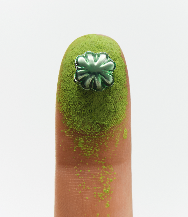 A close up of a green fingertip holding a green clover mini