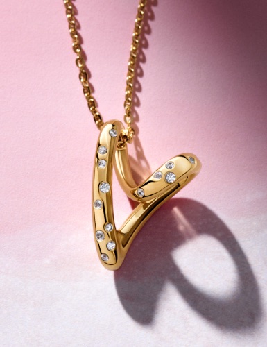 A close-up of a 14k gold-plated heart-shaped necklace on a pink background.