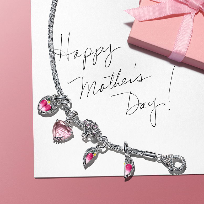 Charms styled on a bracelet over a note that says Happy Mother's Day. 