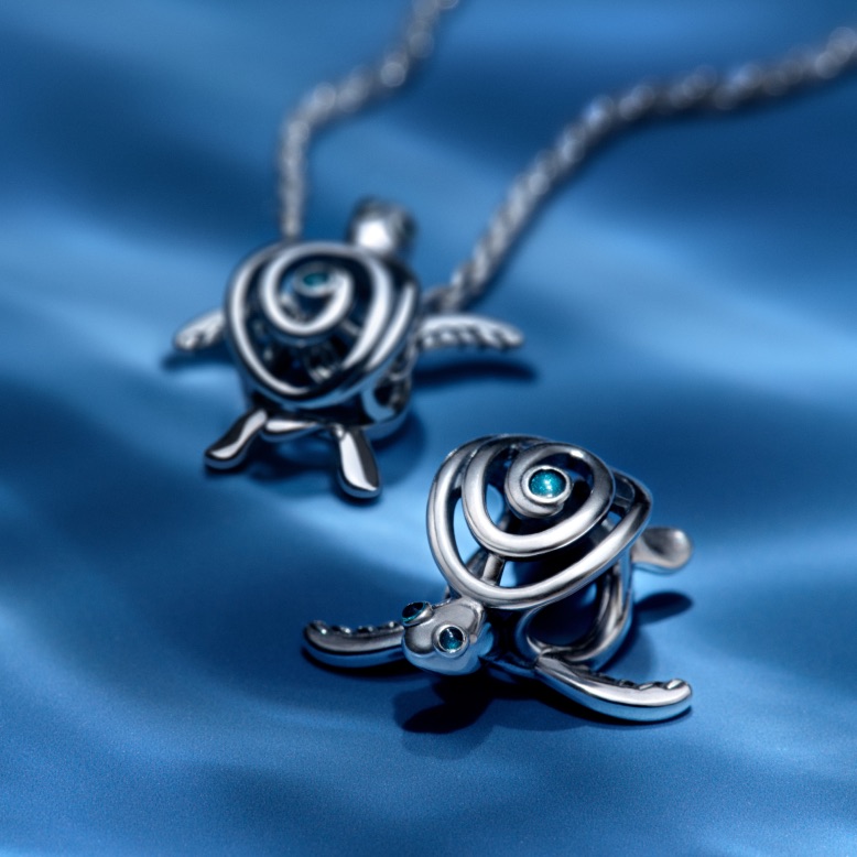 Two sterling silver turtle charms from Pandora Moments on a blue background.