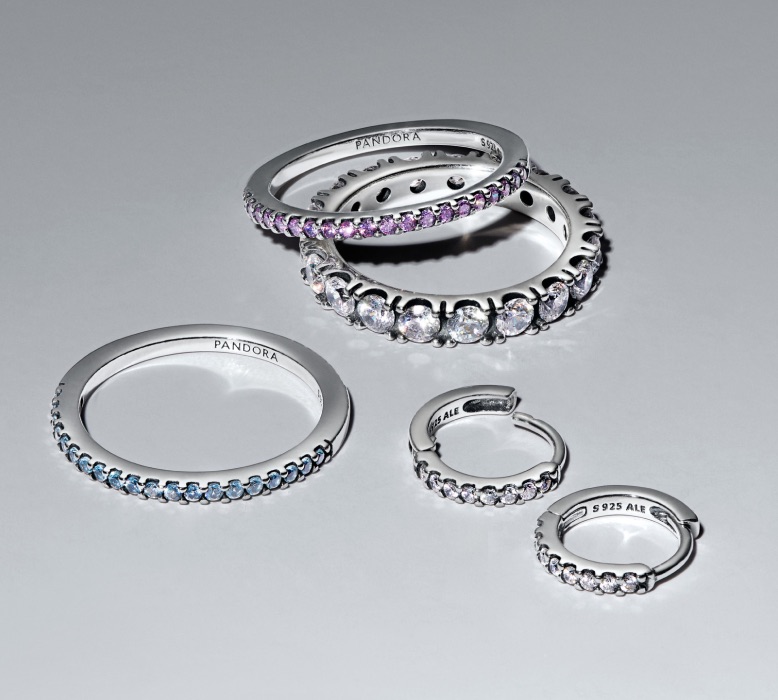 Sterling ezüst Pandora Timeless gyűrűk és karikafülbevalók szürke háttéren elszórva.