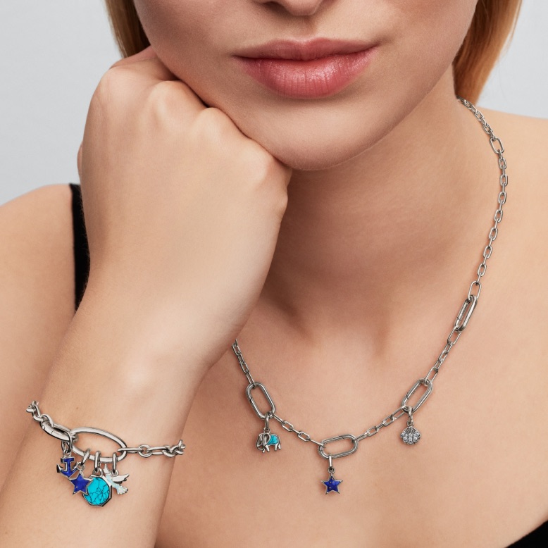 A modell sterling ezüst Pandora ME láncos karkötőt és nyakláncot visel kék charmokkal.