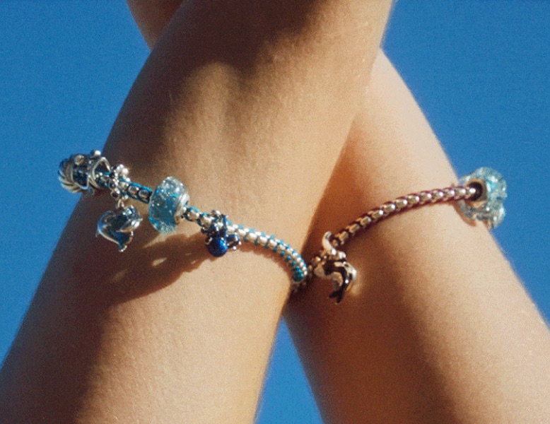 Wrists show colourful Pandora Moments bracelets with charms against a blue sky.