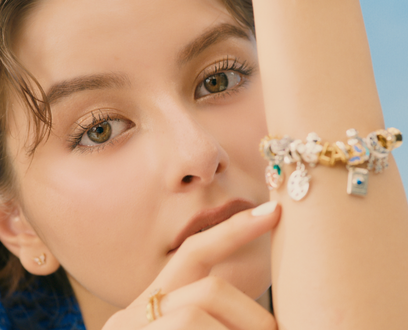 A pair of hands overlap and display an intertwined ring and pearl bracelet.