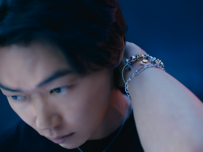 A pair of hands overlap and display an intertwined ring and pearl bracelet.